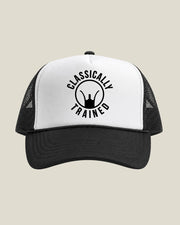 A black and white trucker hat with a black mesh back and a black curved brim. The front panel is white with a black circular graphic that reads 'CLASSICALLY TRAINED' around a silhouette of iron sights.