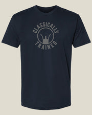 A navy blue short-sleeve t-shirt with an ash grey graphic on the chest that reads 'CLASSICALLY TRAINED' around an iron sight graphic, displayed against a light beige background.