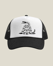 A black and white trucker hat featuring a coiled rattlesnake graphic printed on the white front panel, set against a solid light beige background.
