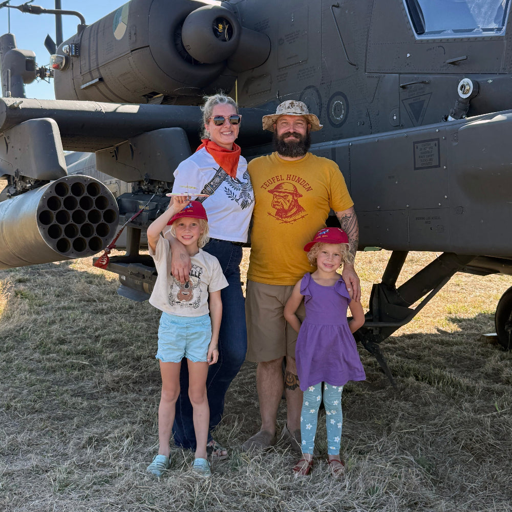Family of four posing in front of a military helicopter on grassy ground.