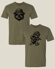 Two olive drab green short-sleeve t-shirts shown on a light beige background. The shirt in the back has a black graphic of a sloth head wearing a boonie hat and smoking a cigar, while the shirt in the front has a sloth soldier with a rifle.