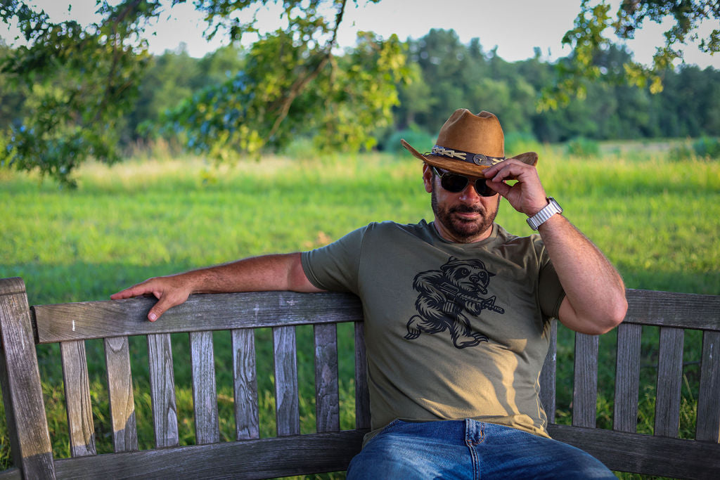 man on bench wearing a cowboy hat and the Smooth is Fast t-shirt in olive drab