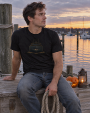 Man wearing the black USS Cyclops T-Shirt in a realistic waterfront lifestyle scene.