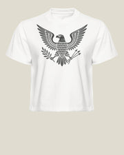 A white cropped boxy t-shirt with a black graphic depicting a heraldic eagle with its wings spread wide, standing on a bundle of arrows and olive branches, paired with black jeans, against a solid light beige background.